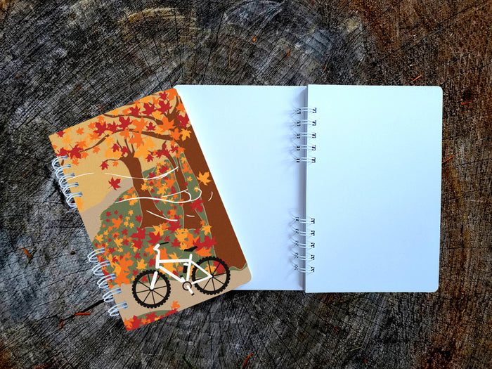 Notebook with autumn-themed cover featuring a bicycle and trees on a wooden surface