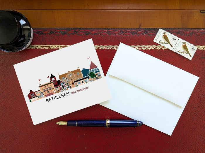 Greeting card with illustration of Bethlehem, New Hampshire, on a red surface with an envelope and pen.