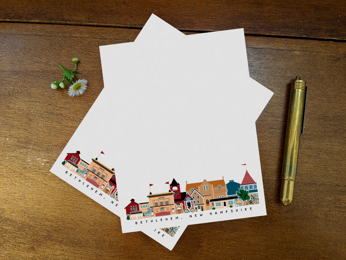 Sheets from notepad with Bethlehem New Hampshire cityscape on a wood surface with pen and flower