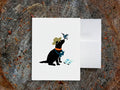 White card with drawing of a dog with binoculars and a hummingbird on a wooden surface.
