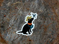 Sticker of a black dog with a hat and binoculars on a wooden surface