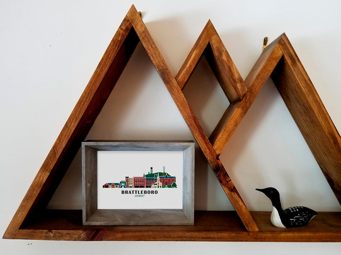 Framed art print on a wooden shelf of buildings arranged in a skyline with the text Brattleboro Vermont