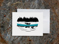 Greeting card with a black dog paddling a blue canoe with wood background