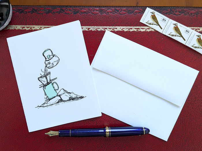 White card with a black ink drawing of pour-over coffee on a red surface with a pen, envelope and stamp.