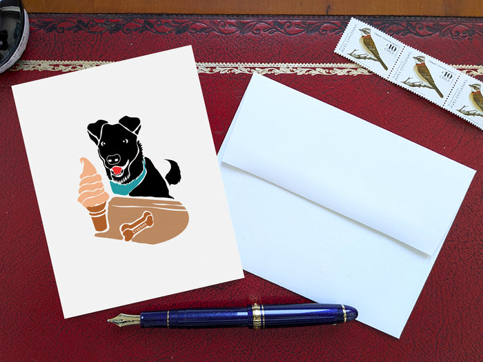 Greeting card with image of black dog looking at a creemee ice cream on a table with a blue pen and envelope and stamps.