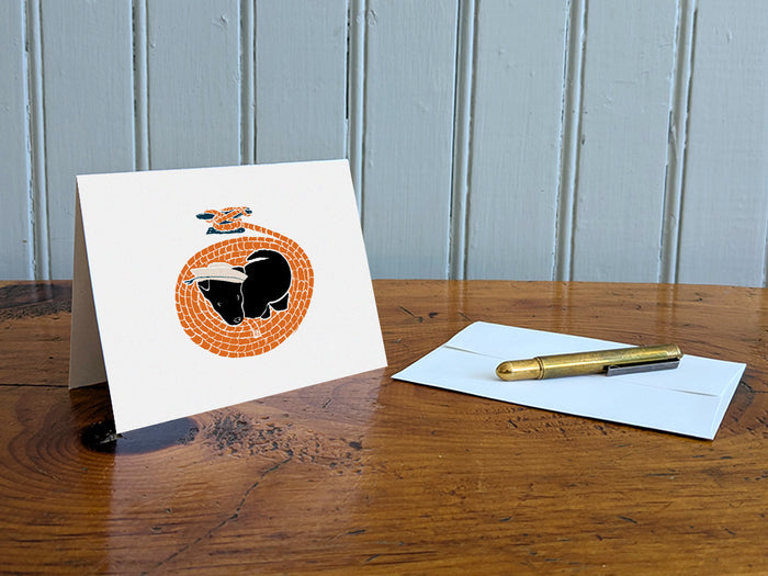 Greeting card with image of a dog with a sailor hat surrounded by rope on a table with gold pen and envelope.
