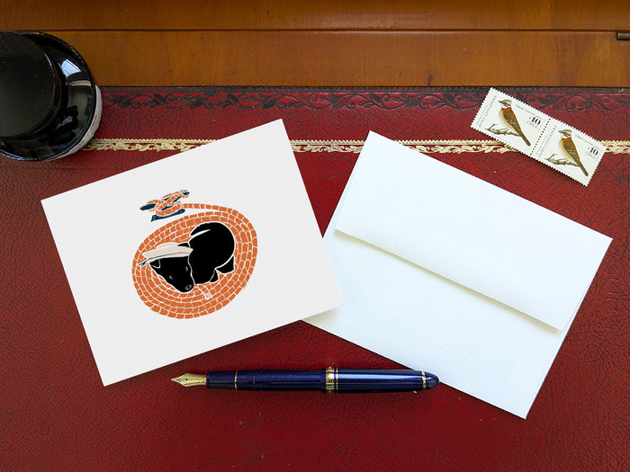 Greeting card with image of a dog with a sailor hat surrounded by rope  on a table with a blue pen and envelope and stamps.