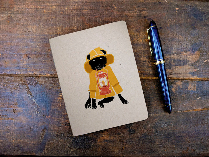 Notebook with a dog illustration in a yellow raincoat on a wooden surface with a blue pen.