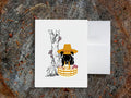 White card with drawing of dog holding basket with mushrooms on a wooden surface.
