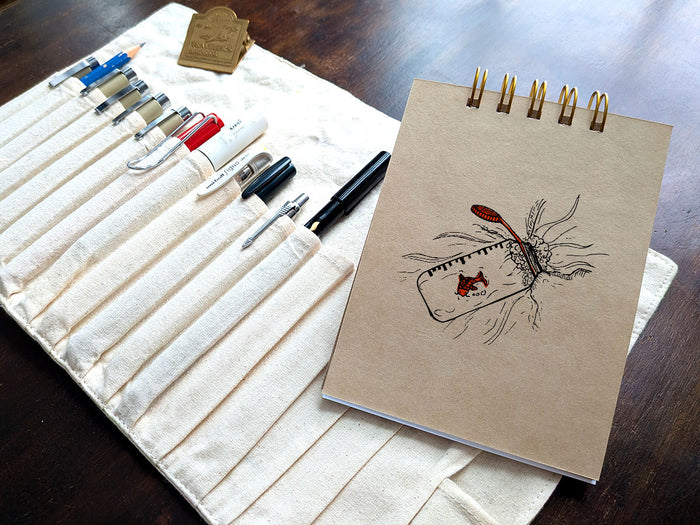 Notebook with a drawing a water bottle with a gold fish, next a pen case on a wood surface.