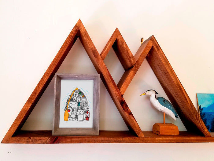 Framed illustration of a canoe filled with gear on a wood shelf.