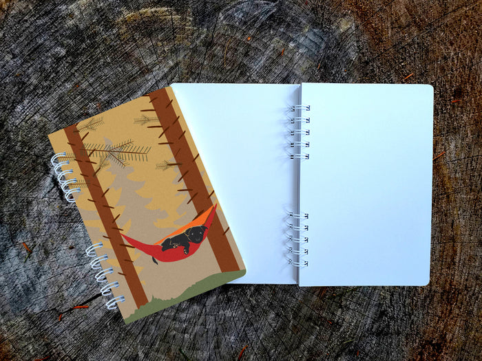 Notebook with a cover featuring a dog in a hammock on a wooden surface.