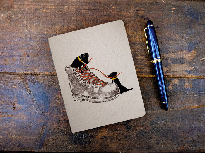 Notebook with illustration of dogs lacing a boot and a pen on a wooden surface