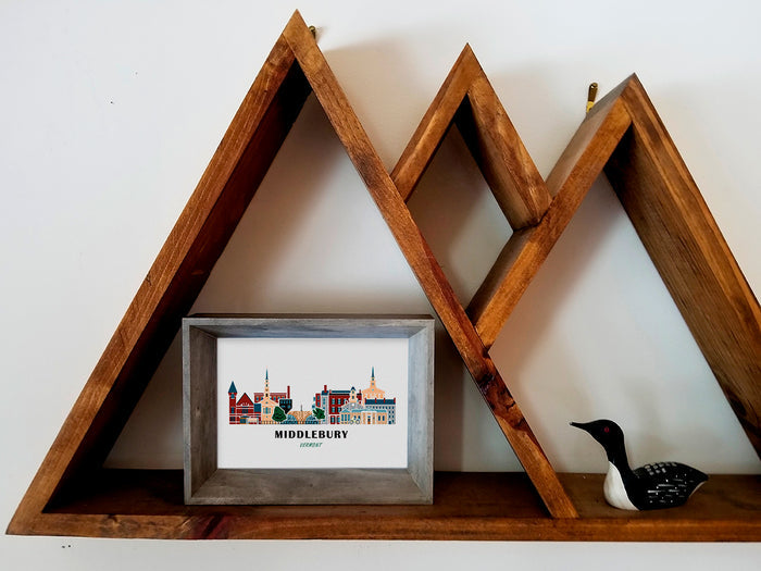 Framed art print on a wooden shelf of buildings arranged in a skyline with the text Middlebury Vermont