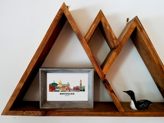 Framed art print on a wooden shelf of buildings arranged in a skyline with the text Montpelier Vermont