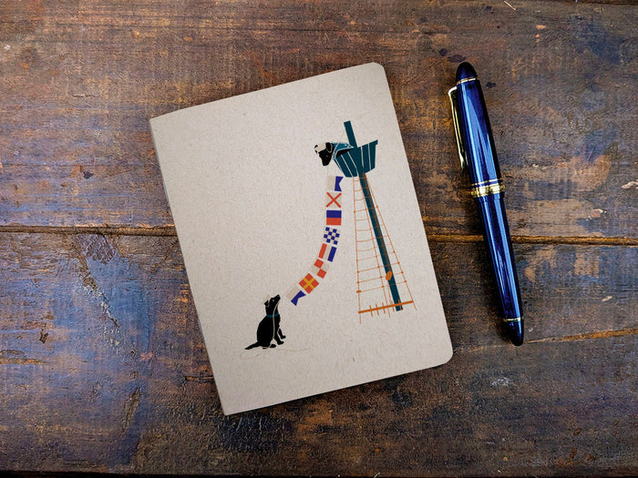 Notebook with illustration of dogs holding nautical flags and pen on a wooden surface