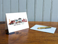 Greeting card with image of buildings arranged in a city skyline with the text Northfield Vermont on a table with gold pen and envelope.
