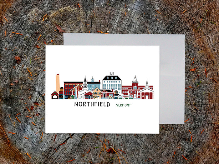 Greeting card with image of buildings arranged in a city skyline with the text Northfield Vermont on a table with envelope.