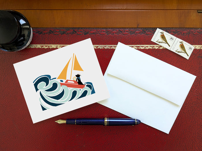 Greeting card with image of a dog in a sailboat on a table with a blue pen and envelope and stamps.