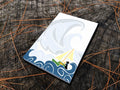 Notepad with illustration of dog sailing big waves on a wood surface.