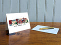 Greeting card with image of buildings arranged in a city skyline with the text Saint Albans Vermont on a table with gold pen and envelope.