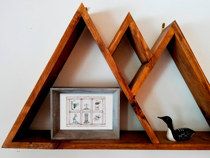 Framed illustration of a window looking into 6 trail scenes - ramen cooking on a camping stove, gear hanging to dry, an outhouse, a trail maker, water bottle, and pour-over coffee - on a wood shelf.