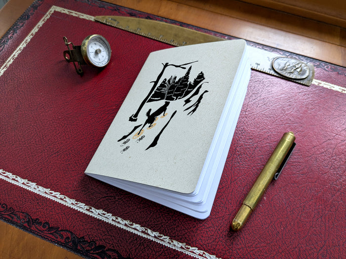 Notebook with dog snowshoeing illustration on a red surface with a pen and small compass.