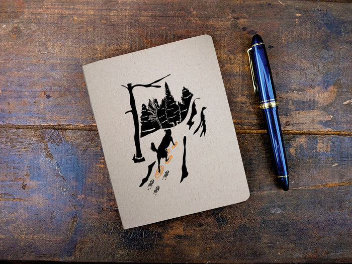 Notebook with a illustration of a dog with snowshoes on a wooden surface with a blue pen.