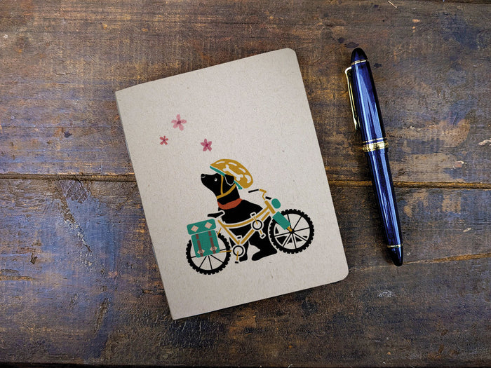 Notebook with a dog on a bicycle illustration and a pen on a wooden surface
