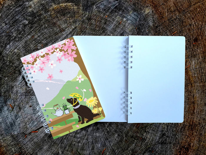 Open notebook with a colorful cover featuring a dog with helmet and cherry blossoms on a wooden surface.