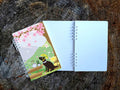 Open notebook with a colorful cover featuring a dog with helmet and cherry blossoms on a wooden surface.