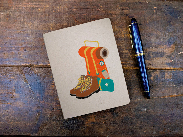 Notebook with a backpacking pack and boot illustration and a pen on a wooden surface