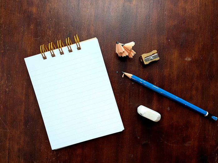 Lined notebook with a blue pencil, eraser, and sharpened pencil on a wooden surface