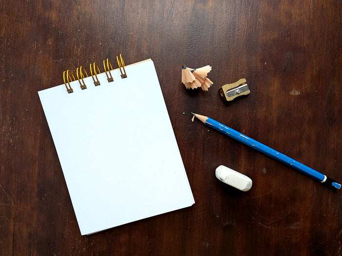 Notebook with a blue pencil, eraser, and sharpener on a wooden surface