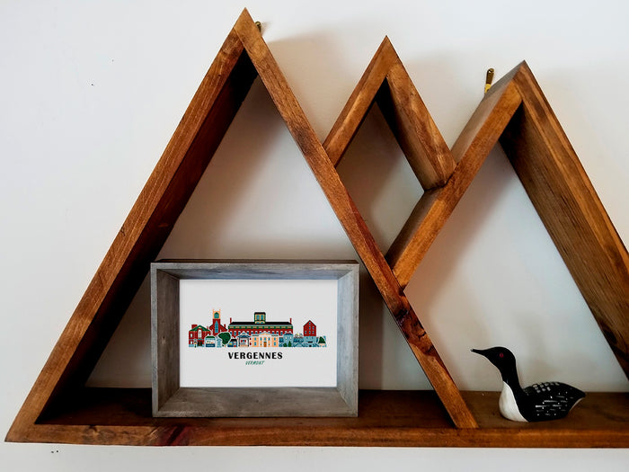 Framed art print on a wooden shelf of buildings arranged in a skyline with the text Vergennes Vermont