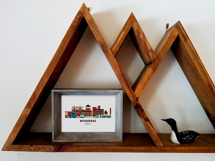 Framed art print on a wooden shelf of buildings arranged in a skyline with the text Winooski Vermont